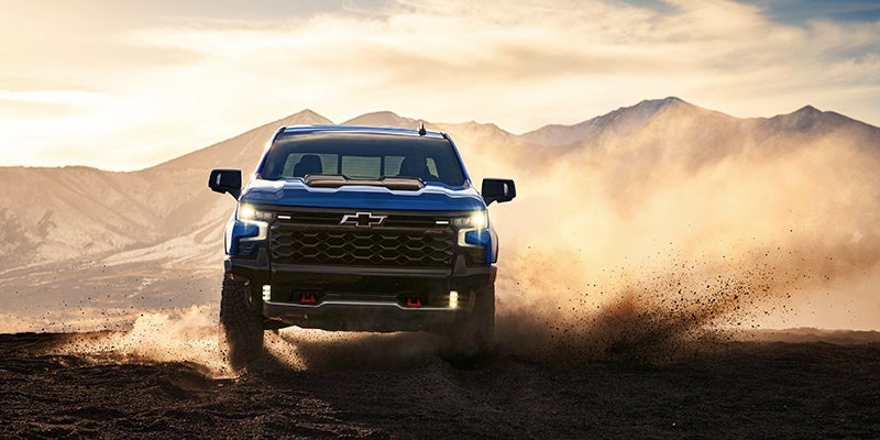 Blue Chevrolet Silverado driving on a dirt road with mountains in the background
